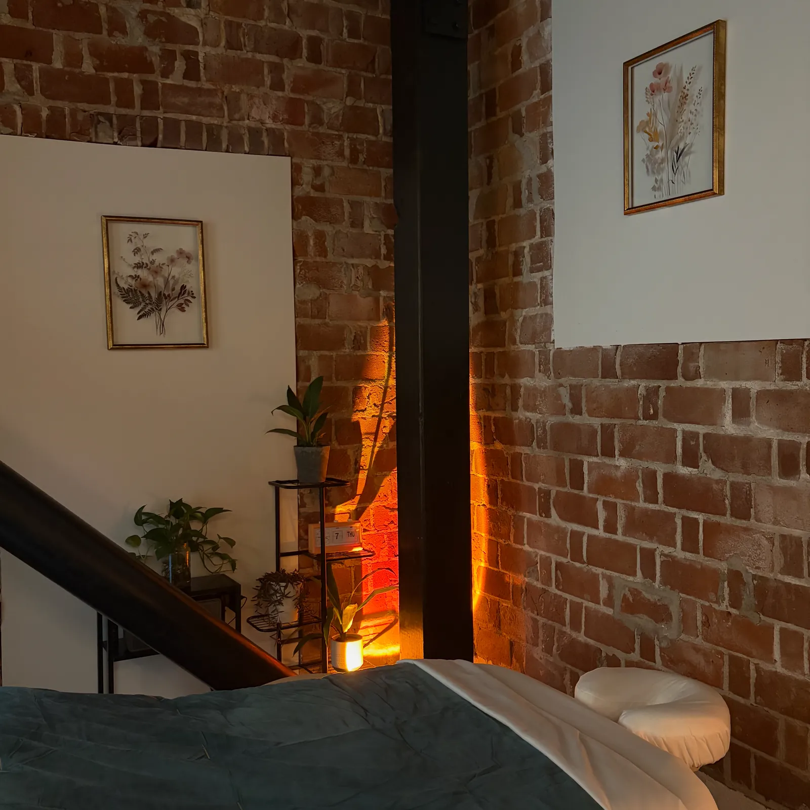 A massage room with exposed brick, leafy plants, and warm orange light
